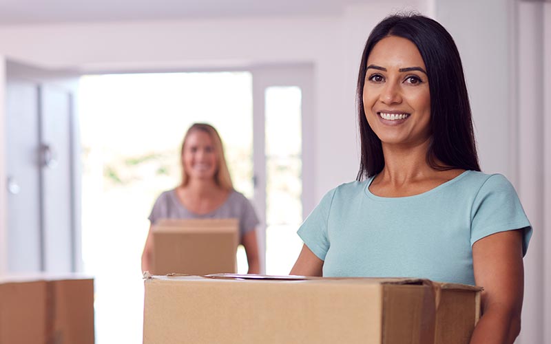 Two women moving boxes into their new home