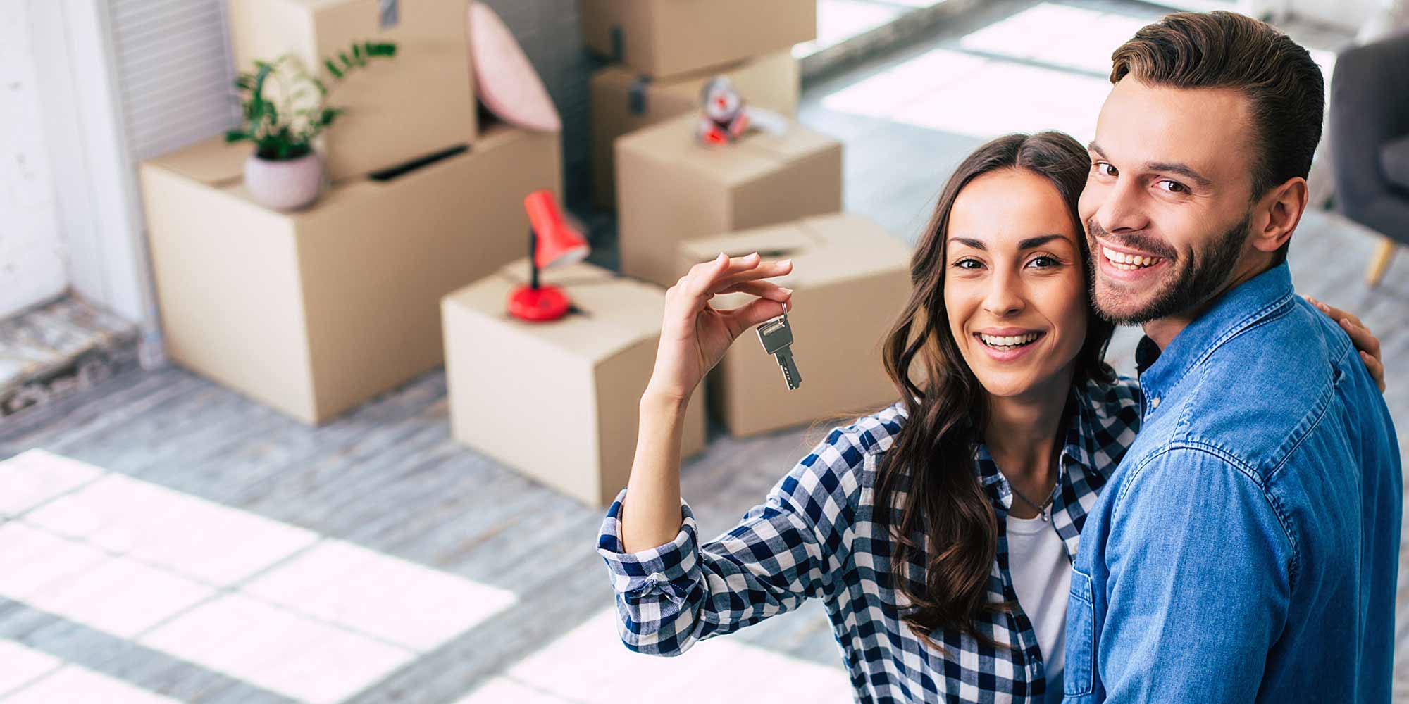 Young couple in their new home surrounded by boxes and holding a set of house keys
