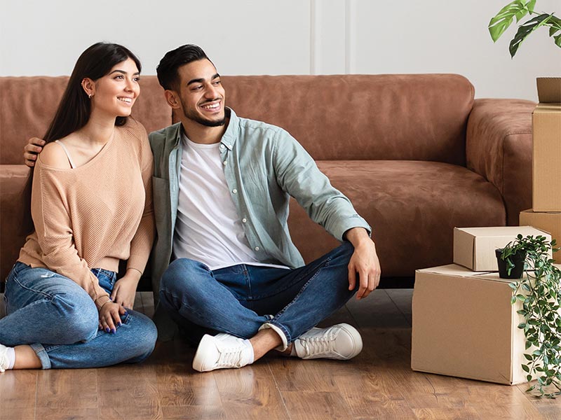 Couple sat on the floor of their new home surrounded by boxes